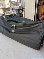 Side view of black rolling duffle showing zippered exterior pocket and carry handles