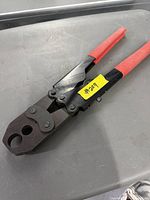 Dual jaw PAX crimping tool with red handles laid flat