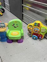 Wide shot of both items: green Fisher-Price chair and yellow VTech activity panel