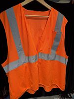 Front view of orange high-visibility mesh safety vest with reflective stripes and chest pocket, hanging on hanger