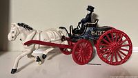 Side view of white horse, red shafts, black carriage with gold trim and driver, red wheels