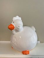 Front left view of white ceramic chicken coin bank
