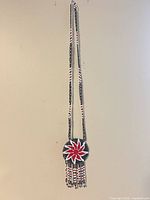 Full view of beaded necklace hanging to show length, medallion and fringe
