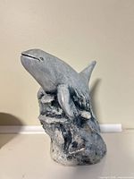 Front view of volcanic ash orca sculpture showing breaching pose and base texture