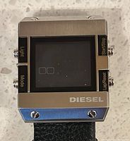 Front view showing square stainless steel case, digital display, button labels