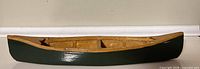 side profile of wooden canoe showing green hull and natural wood interior