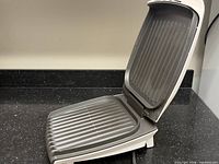 Grill open showing ribbed non-stick cooking plates and hinge