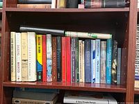 Shelf view of approximately two dozen hardcovers with dust jackets, showing spines and general wear