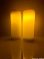 Front view of two illuminated ivory wax flameless pillar candles