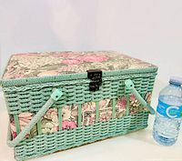 Front view of mint wicker basket with floral lid next to water bottle for scale