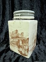 Front and side view of square ceramic canister showing scenic castle design and grey lid