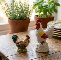 Rooster figurine and hen egg cup on tabletop near plants