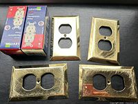 Five brass outlet covers and two boxed Leviton receptacles front view