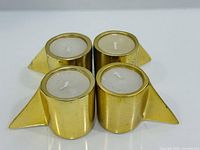 Front view of four brass-plated tealight holders with candles