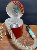Hair dryer in red case with hose, brush attachment visible