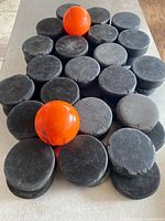 Pile of black hockey pucks with two orange balls on top