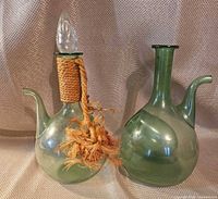 Both green glass cruets side by side showing overall form, spouts, stopper, rope wrap