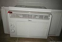 Front view of Midea window AC showing grille, brand logo, control panel and accordion panels