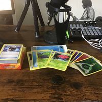 Stack of Pokémon cards on deck box with metallic coin visible