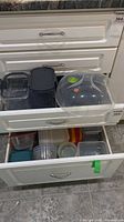 Drawers containing assorted clear plastic food storage containers with colored lids