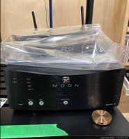 Front view of MOON MiND 2 showing logo, indicator LEDs, control buttons, attached antennas, protective plastic cover and brass puck