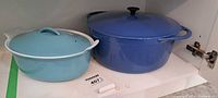 Both Dutch ovens side by side on shelf showing exterior color and lids