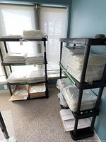 Two black plastic utility shelves with packaged contents on them