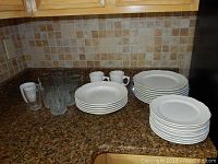 Overview of bowls, plates, glasses, and mugs arranged on a brown granite countertop with tile backsplash.