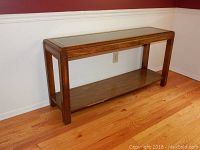 Full view of the rectangular glass top console sofa table showing wood frame and woven accent beneath the glass