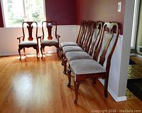 Set of six wooden dining chairs with velvety corduroy upholstery in a row against a burgundy wall, showing full view of chairs and their design distinguishing armrest and side chairs.