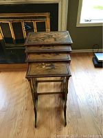 Four wooden nesting tables stacked, showing painted tops with Asian scenes and visible wear.