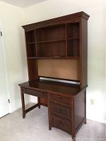 Front angle view of wooden desk with attached hutch showing shelving, drawers, and surface with light scratches.