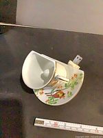 Overall view of porcelain night light showing teacup and saucer design with bird motif and plug prongs