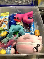 Plastic bin showing assorted toys including large ponies, diecast car box, wooden giraffe toy box, pig coin pouch and mini figures