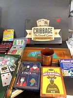 Assorted boxed card and board games with wooden cribbage board, dice cup and loose dice visible