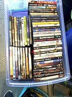 Top view of plastic bin containing roughly 48 DVD movies, spines readable