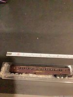 Full view of maroon N scale passenger coach in plastic tray with ruler showing length