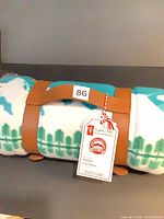 Rolled blanket secured by tan strap, hang tag attached