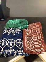 All three lightweight throws folded, showing green sunburst, navy sun face, rust tribal patterns