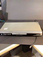 Front view of Sylvania DVD player showing disc tray, buttons, power cord