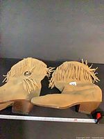 Full view of both tan suede fringe ankle boots lying side by side