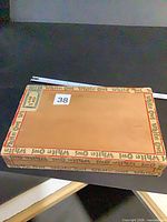 Top of closed White Owl cigar box showing plain tan cover with red branded border and tax stamp