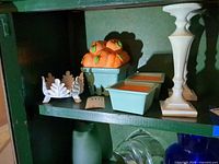 Shelf view showing peach candle, white leaf candle holder, two aqua candles, off-white pillar holder