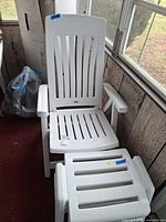 White plastic armchair with slatted back and seat, matching stool in foreground