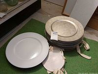 Stack of brushed silver chargers next to white charger, size perspective