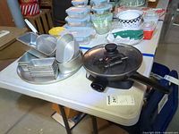 Electric fry pan with glass lid and surrounding bakeware on table