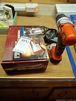 Boxed Strike Force impact wrench beside Black & Decker cordless driver, charger cable visible