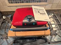 Closed grill with manual on top and drip tray below