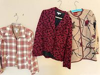 Three garments on hangers: plaid jacket, magenta blazer, beige embroidered cardigan