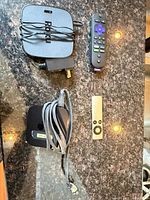 Roku unit, power adapter, Roku remote, Apple TV, Apple Remote arranged on countertop